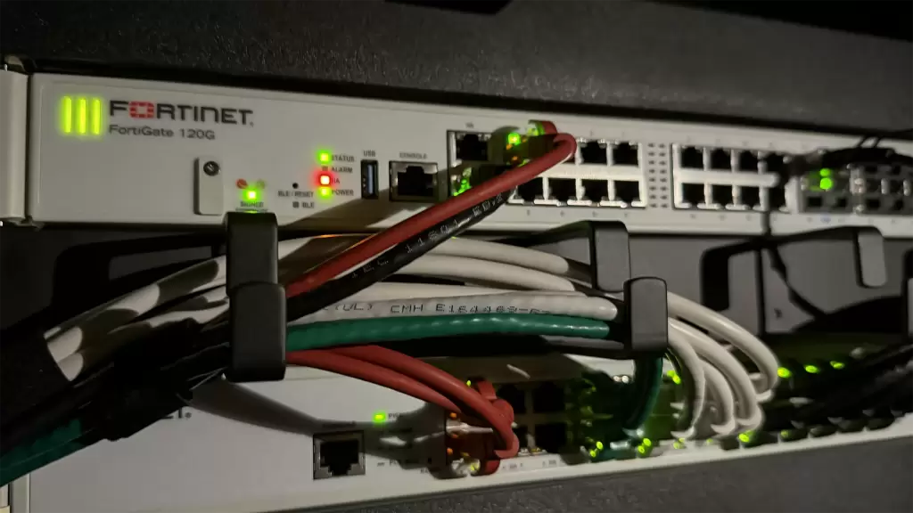 FortiGate 120G-firewall met groene statuslampjes in een netwerkrack, aangesloten op een switch.