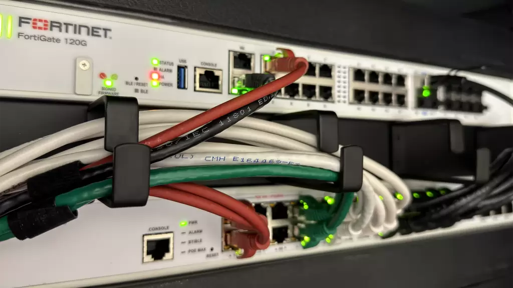 FortiGate 120G-firewall boven een switch in een netwerkrack, met net weggewerkte netwerkbekabeling.