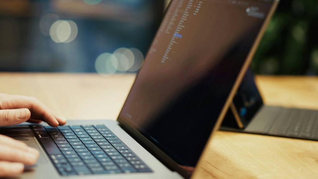 Handen aan een laptop met programmeercode op het scherm.