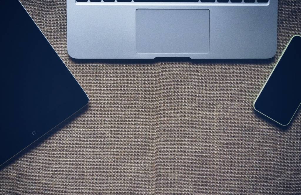 Laptop, tablet en smartphone liggen samen op een bureau.