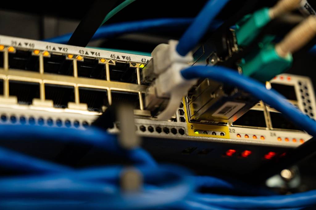 Netwerkswitch met aangesloten blauwe datakabels en brandende statuslampjes.