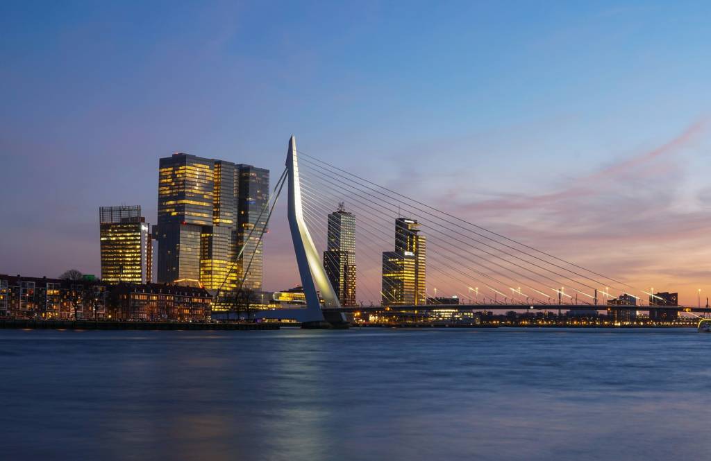 Skyline van Rotterdam bij avond met de Erasmusbrug en verlichte kantoorgebouwen.