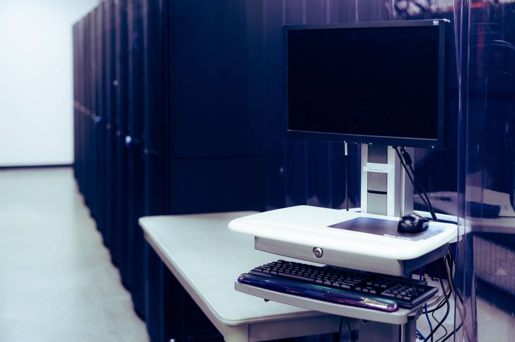 Serverruimte met donkere serverkasten en een beheerconsole met monitor en toetsenbord.